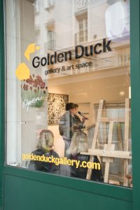 Exterior view through the window of the Golden Duck Gallery and Art Space during the opening reception of the ArtBIAS IV exhibition.